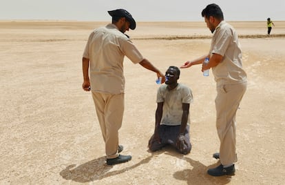 Two Libyan border agents give water to a migrant of African descent in a desert area on the Tunisia-Libya border, in July 2023.