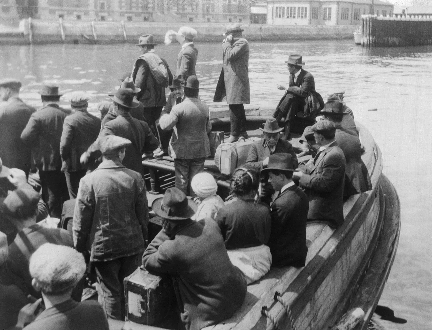 This black-and-white historical photo from the 1920s shows the deck of a small boat crowded with people as it floats on a river.