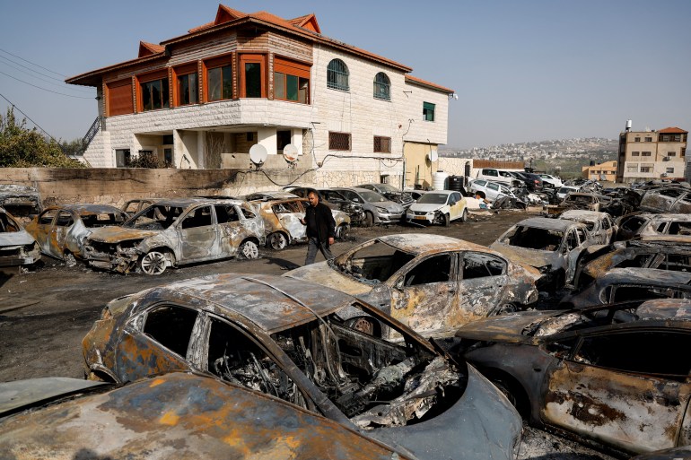 A man walks among cars burnt in an attack by Israeli settlers
