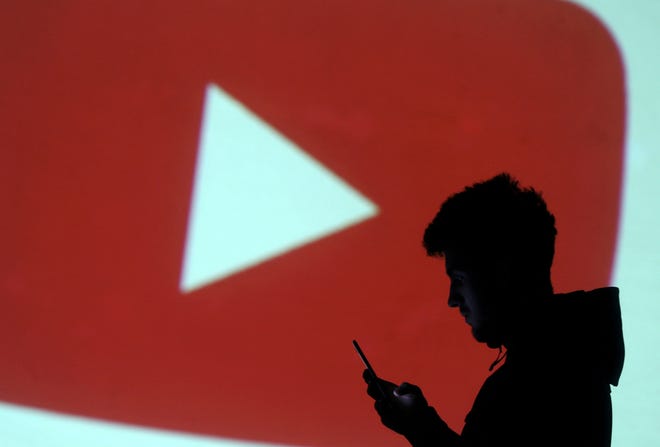FILE PHOTO: A silhouette of a mobile user is seen next to a screen projection of Youtube logo in this picture illustration taken March 28, 2018. REUTERS/Dado Ruvic/Illustration/File Photo