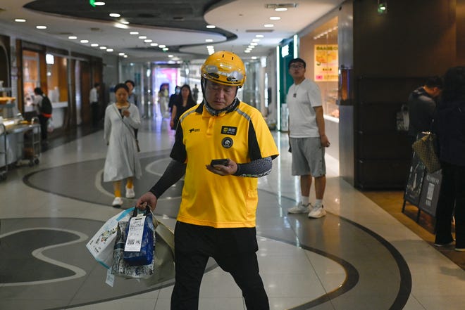 A food delivery worker looks at his mobile phone while carrying items to be delivered at a mall in Beijing on July 10, 2024.