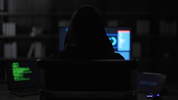 Back view of young adult man with a hood coding a virus to hack the security system and steal the victim's information. A male black hat hacker is hacking the system for cyber theft in dark theme.