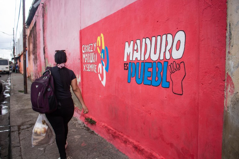 A woman walks past slogans painted on a wall next to a sidewalk, advertising Maduro's campaign.